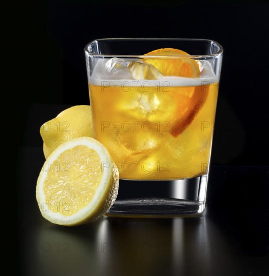 Cocktail in a tumbler on ice with orange slice and lemons as garnish against a black background, studio shot