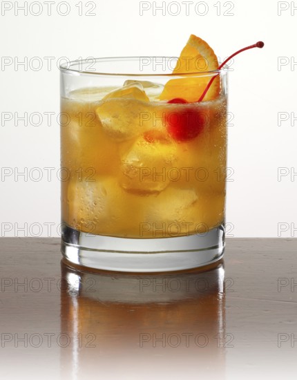 Cocktail in a tumbler on ice with half an orange slice and cocktail cherry as garnish against a white background, studio shot