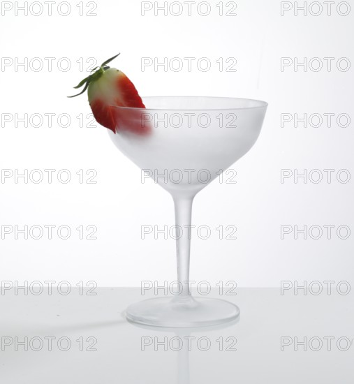 Empty, frosted cocktail glass with strawberry garnish against a white background, studio shot