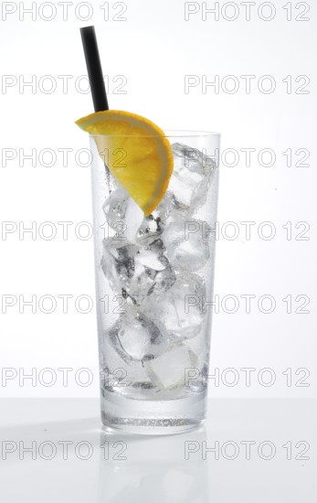 Betautes long drink glass, filled with ice cube cubes, half an orange slice as garnish, in front of a white background, studio shot