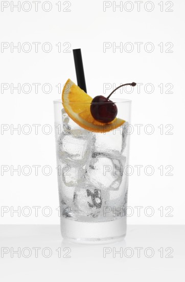 Betautes long drink glass, filled with ice cube cubes, half orange slice and cherry as garnish, in front of white background, studio shot