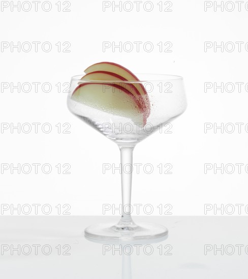 Frosted empty cocktail glass with apple slices as garnish against a white background, studio shot