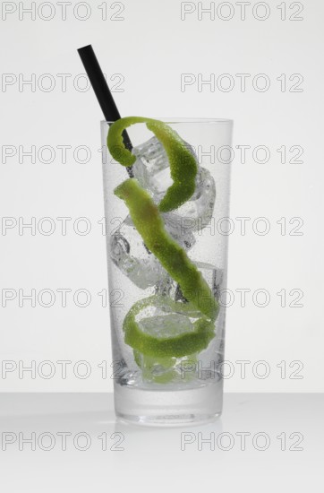 Betautes cocktail glass, filled with ice cube cubes, lime zest as garnish, in front of a white background, studio shot