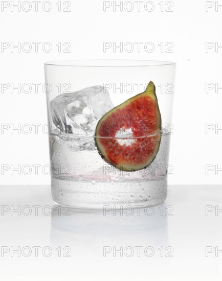 White rum in a tumbler on ice with a fig slice as garnish against a white background, studio shot