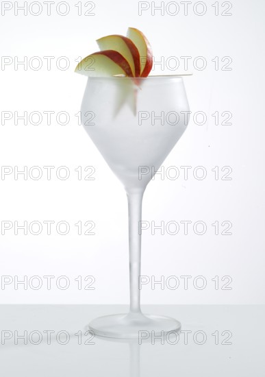 Empty, frosted cocktail glass with apple slices as garnish against a white background, studio shot