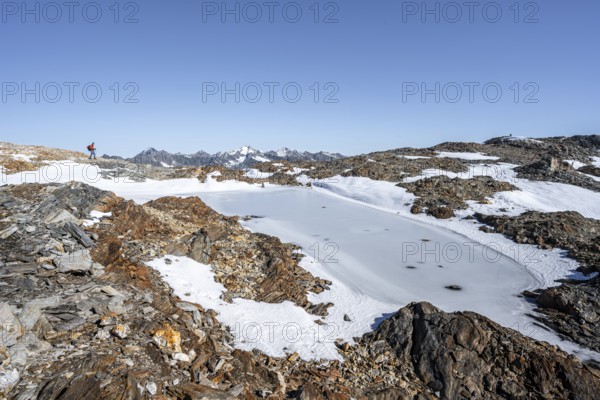 Mountaineer in rocky high mountain landscape, frozen small mountain lake, mountain tour from the Wilder Freiger to the Red Ridge, Stubai Alps, South Tyrol, Italy