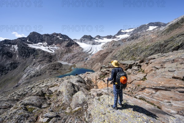 Mountaineer on hiking trail, view of blue glacial lake in rocky mountain landscape, behind Königshofspitz, Schwarzwandspitz and glacier Ãœbeltalferner, descent from summit Roter Grat, Stubai Alps, South Tyrol, Italy