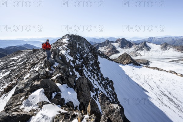 Mountaineer on narrow rocky ridge at the summit of Wilder Freiger, picturesque high mountain landscape with snow, view of glacier Ãœbeltalferner and rocky mountain peaks Königshofspitz, Stubai Alps, South Tyrol, Italy