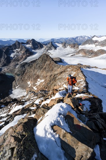 Mountaineer on a rocky ridge on the Wilder Freiger summit, behind him Signal summit and Becher summit with Becherhaus, picturesque high mountain landscape, view of Ãœbeltalferner glacier and rocky mountain peaks Königshofspitz and Sonklarspitze, Stubai Alps, South Tyrol, Italy