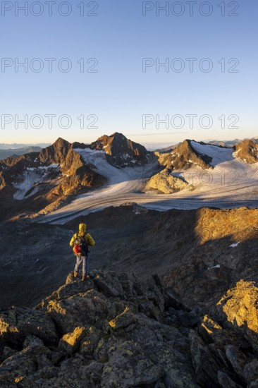 Mountaineers in front of a picturesque high mountain landscape at sunrise with alpenglow, glacier and rocky mountain peaks in the morning light, view at the Becher on mountain peak Königshofspitz and glacier Ãœbeltalferner, Stubai Alps, South Tyrol, Italy