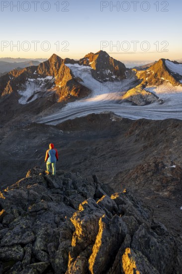 Mountaineer in front of picturesque high mountain landscape at sunrise with alpenglow, glacier and rocky mountain peaks in the morning light, view at the cup on mountain peak Königshofspitz and glacier Ãœbeltalferner, Stubai Alps, South Tyrol, Italy