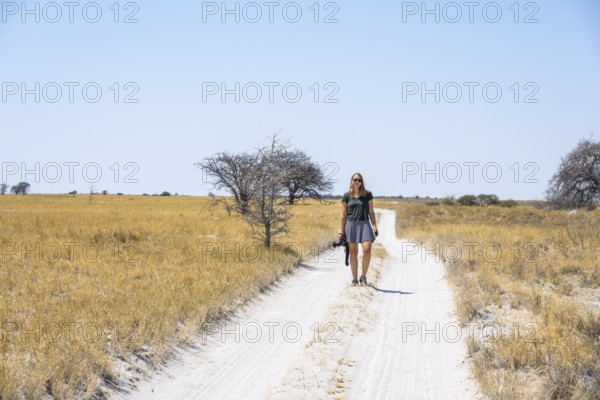 Tourist with camera on a sandy track between yellow dry grass, Makgadikgadi salt pans, Botswana