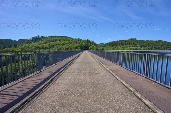 A straight view along a dam with a view of wooded land under a clear sky, Oleftalsperre, Hellenthal, Eifel, North Rhine-Westphalia, Germany