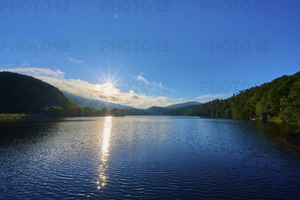 The sunny morning mood is reflected golden on the water of the lake, surrounded by peaceful hills and trees, summer, Rursee, Obersee, Rurberg, Simmerath, Eifel National Park, Eifel, North Rhine-Westphalia, Germany