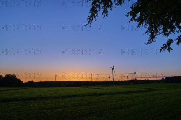 Silhouettes of wind turbines rise into the colourful morning sky as the sun rises behind the meadow, summer, Rohren, Monschau, Eifel, North Rhine-Westphalia, Germany