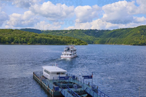 A departing passenger ship, on a large lake under a cloudy sky, summer, Rursee, Rurtalsperre, Heimbach, Simmerath, Eifel National Park, North Rhine-Westphalia, Germany
