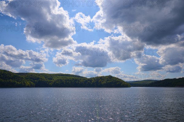 Blue sky with clouds over a calm, glittering lake and wooded hills, summer, Rursee, Rurtalsperre, Simmerath, Eifel National Park, North Rhine-Westphalia, Germany