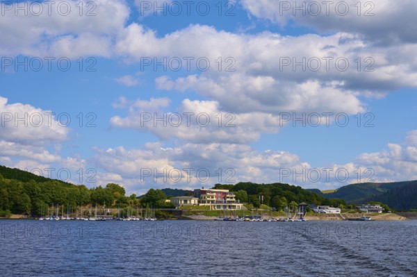 Buildings and boats along a lake in front of a sky with white clouds, summer, Rursee, Rurtalsperre, Heimbach, Simmerath, Eifel National Park, North Rhine-Westphalia, Germany