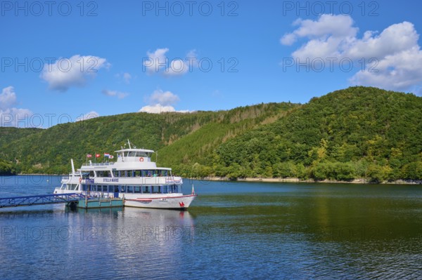 Passenger ship anchored at the jetty, in front of green hills under a blue sky, summer, Rursee, Rurberg, Simmerath, Eifel National Park, North Rhine-Westphalia, Germany