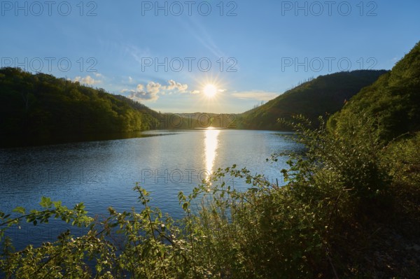 Sunset over a calm lake with green hills in the background, summer, Rursee, Obersee, Simmerath, Eifel National Park, North Rhine-Westphalia, Germany