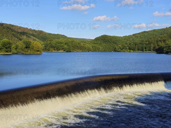 Clear water flows over a dam in a lake surrounded by forests with a blue sky, summer, Rursee, Obersee, Rurberg, Simmerath, Eifel National Park, North Rhine-Westphalia, Germany