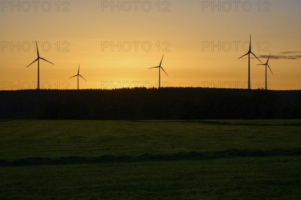 Silhouette of wind turbines at sunrise, over a green field, summer, Rohren, Monschau, Eifel, North Rhine-Westphalia, Germany