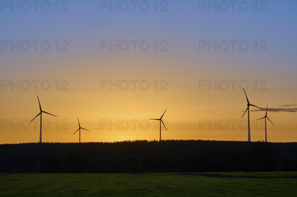 Wind turbines in front of an orange-coloured sky at sunrise, above a meadow, summer, Rohren, Monschau, Eifel, North Rhine-Westphalia, Germany