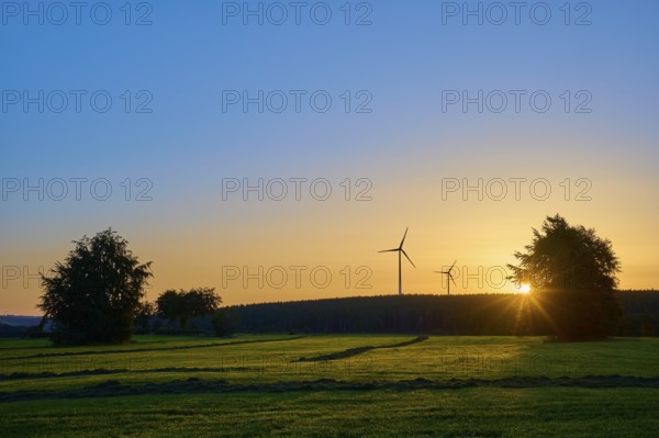 Wind turbines and trees at sunrise, the orange-coloured sky radiates warmth, summer, Rohren, Monschau, Eifel, North Rhine-Westphalia, Germany