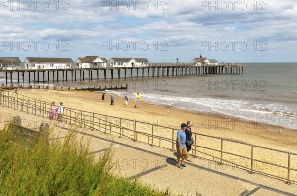 People walking on seafront promenade next to sandy beach and pier, Southwold, Suffolk, England, UK