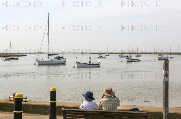 People looking out from quayside at boats moored in harbour, River Ore, Orford, Suffolk, England, UK