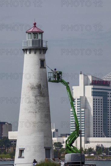 Detroit, Michigan - A worker on a lift paints the Milliken State Park Lighthouse. The lighthouse is on the Detroit River, near downtown Detroit. Caesars Casino hotel is across the river in Canada