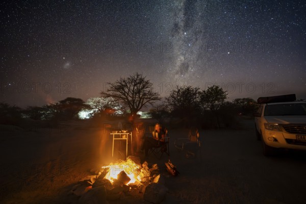 Tourists sitting around a campfire next to their off-road vehicle at night, night shot with starry sky and Milky Way, Kubu Island (Lekubu), Sowa Pan, Makgadikgadi Salt Pans, Botswana