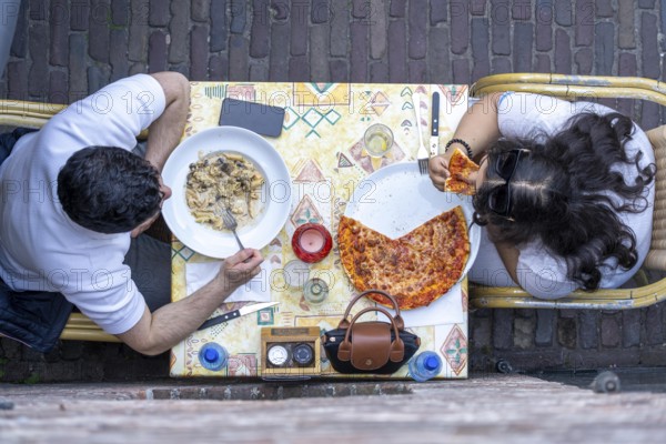 Man and woman sitting in an Italian restaurant eating pizza and pasta, symbolic picture