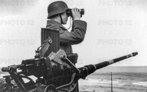 German WWII soldier looking over the North Sea with binoculars next to anti-aircraft gun at WW2 Atlantic Wall, Raversijde, West Flanders, Belgium