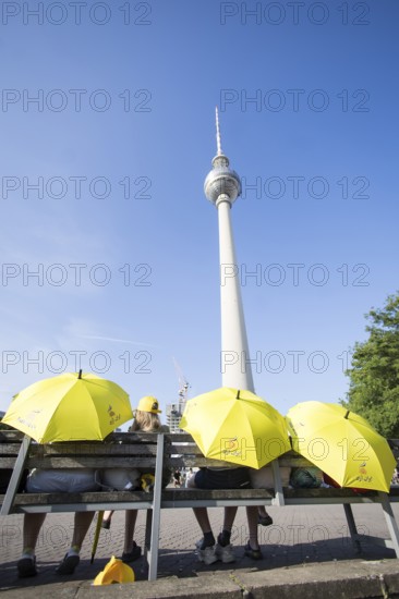 Several people sit with yellow Free Iran umbrellas in front of the television tower on Alexanderplatz in Berlin on 21 June 2025