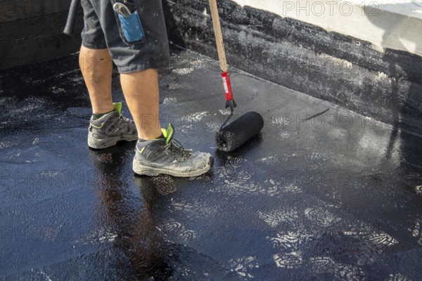 Flat roof waterproofing: Roofer applying the bitumen primer