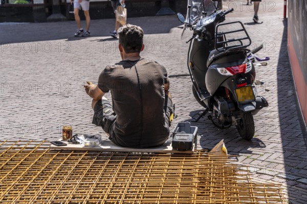 Construction worker taking a lunch break, sitting on wire mats in front of the building site