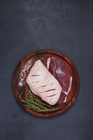 Fresh raw duck breasts, on a wooden chopping board, with herbs and spices, no people