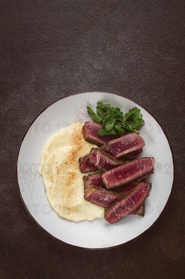 Sliced steak, served with creamy mashed potatoes, and fresh herbs, no people