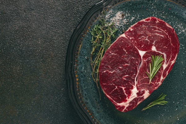 Steak made from fresh beef, with herbs and various spices, on a plate, ready to cook, there are no people
