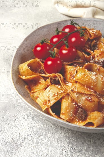 Pappardelle pasta with bolognese sauce, topped with parmesan cheese and cherry branch, homemade, no people