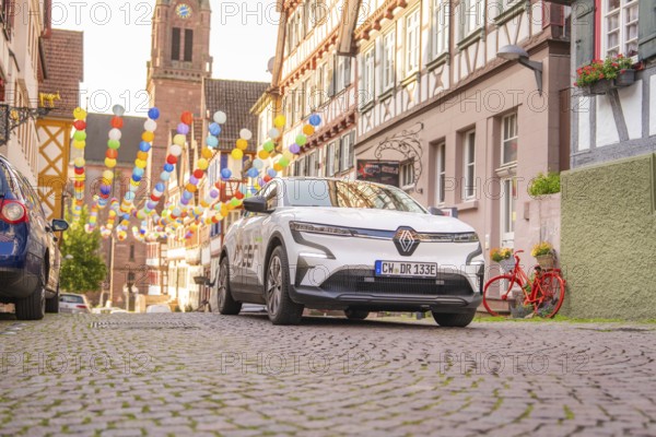 A Renault stands on a colourful street with half-timbered houses and balloons, Deer E, car sharing, electric car, Calw, Black Forest
