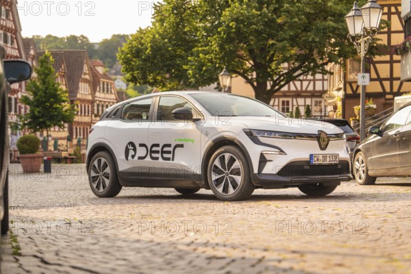 Car in the old town centre next to half-timbered houses, friendly summer atmosphere and tall greenery in the background, Deer E, car sharing, electric car, Calw, Black Forest
