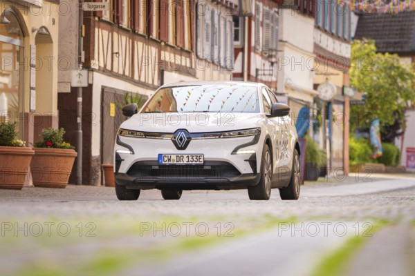 A white electric car drives through a narrow cobbled street with colourful shutters in the town, Deer E, car sharing, electric car, Calw, Black Forest
