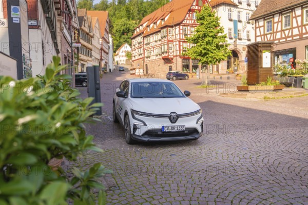 A car on a cobbled street surrounded by traditional half-timbered houses and green vegetation, Deer E, car sharing, electric car, Calw, Black Forest