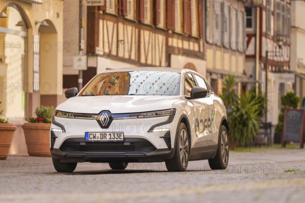 A car drives along a cobbled street, lined with traditional half-timbered houses, in bright sunlight, Deer E, car sharing, electric car, Calw, Black Forest