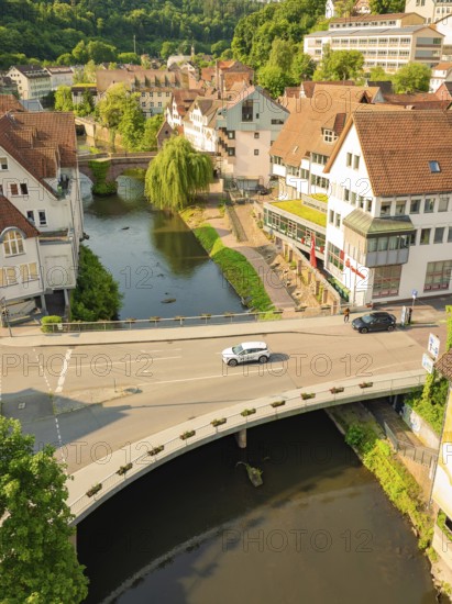 A car drives over a bridge that crosses a river in a charming urban landscape with green surroundings, Deer E, car sharing, electric car, Calw, Black Forest