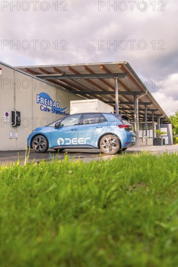 Electric car near an outdoor swimming pool, surrounded by grass and under a cloudy sky, Deer E, car sharing, electric car, Calw, Black Forest