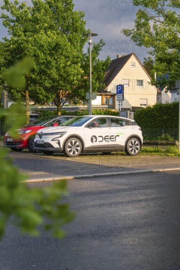 A white electric car parked in a car park in front of a house in a green residential area, Deer E, car sharing, electric car, Calw, Black Forest