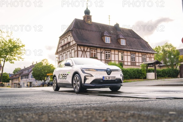 A white electric car drives past a traditional building in a historic town, Deer E, car sharing, electric car, Calw, Black Forest